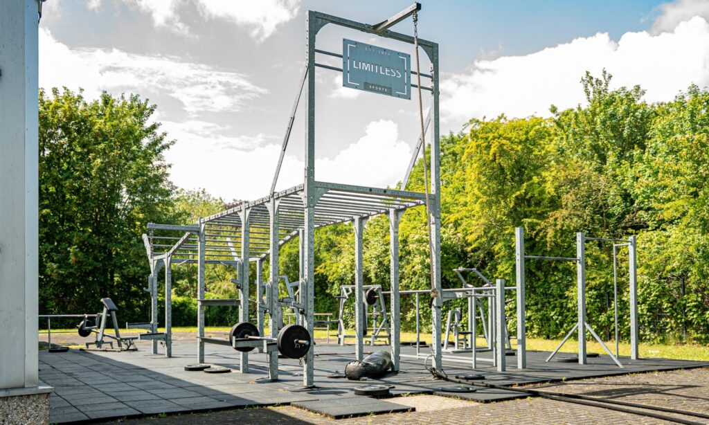 Outdoor Gym Gesamtansicht mit Limitless Sports Schild, Racks und Freihanteln vor grünem Baumhintergrund in Herten